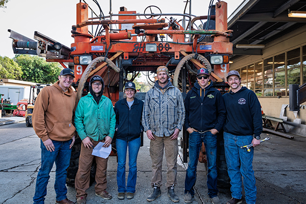 Cal Poly College of Agriculture, Food and Environmental Sciences students stand in front of a prototype agave harvester. 