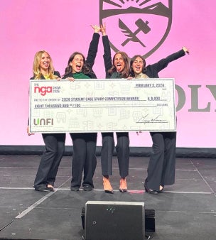 Four Cal Poly students raise their hands in celebration while holding an oversized check. 