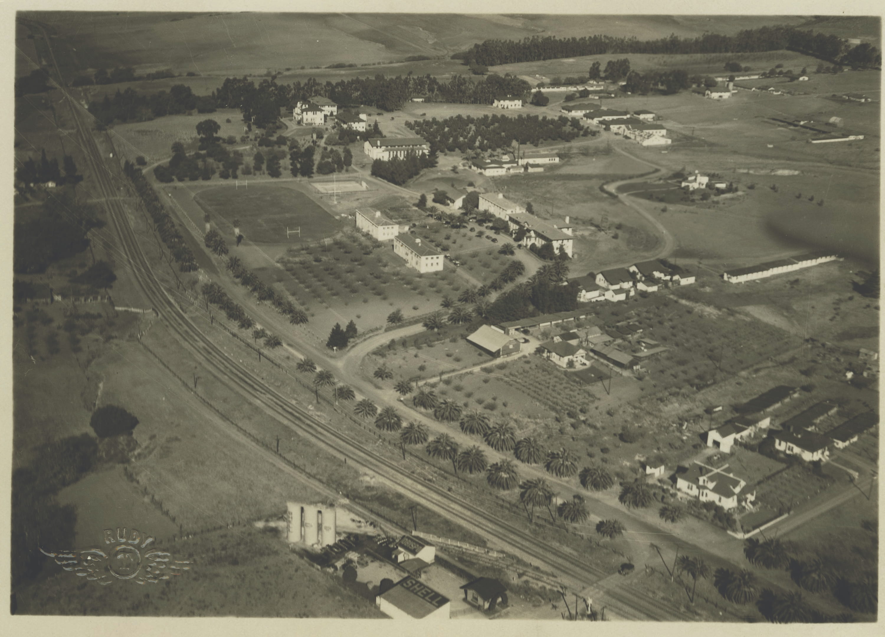 Historic aerial photograph of an agricultural college campus and surrounding farmland, showing early academic buildings, orchards, athletic fields, railroad tracks, and rural landscapes in the early twentieth century.