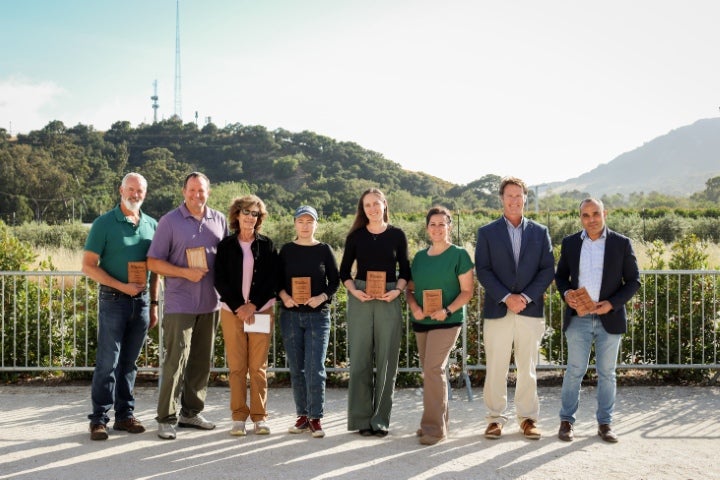 Faculty and staff award recipients posing outdoors with recognition plaques, standing together in front of a scenic landscape with hills and greenery in the background.
