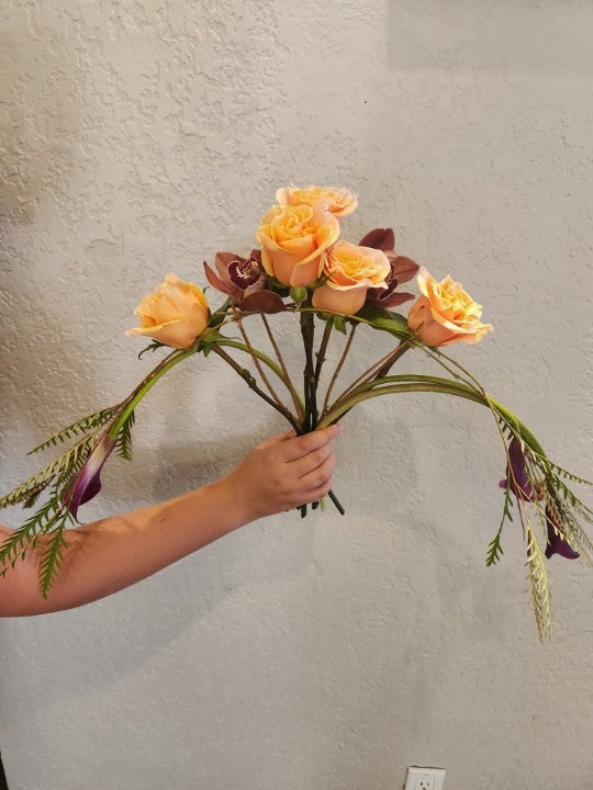 Hand holding an elegant floral arrangement featuring roses and decorative greenery created for a floral design activity or showcase.