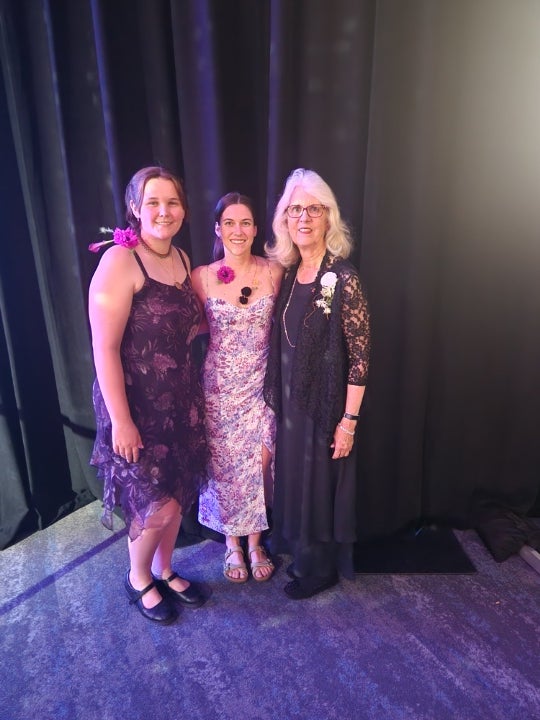 Three individuals posing together at a formal event or banquet while wearing floral accessories and evening attire.