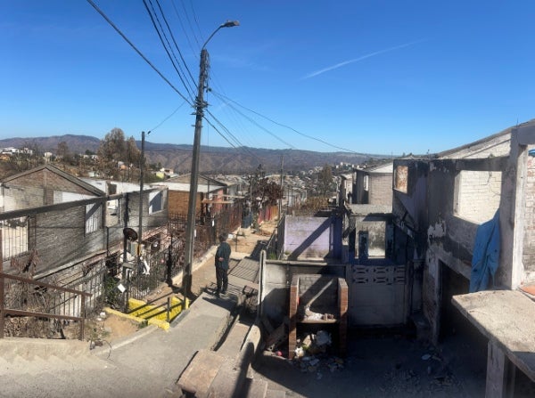 View of a hillside neighborhood with homes, utility lines, and narrow streets, showing an urban residential community under a clear blue sky with mountains in the distance.