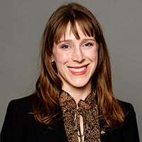Professional headshot of a woman with red hair wearing business attire against a studio background.