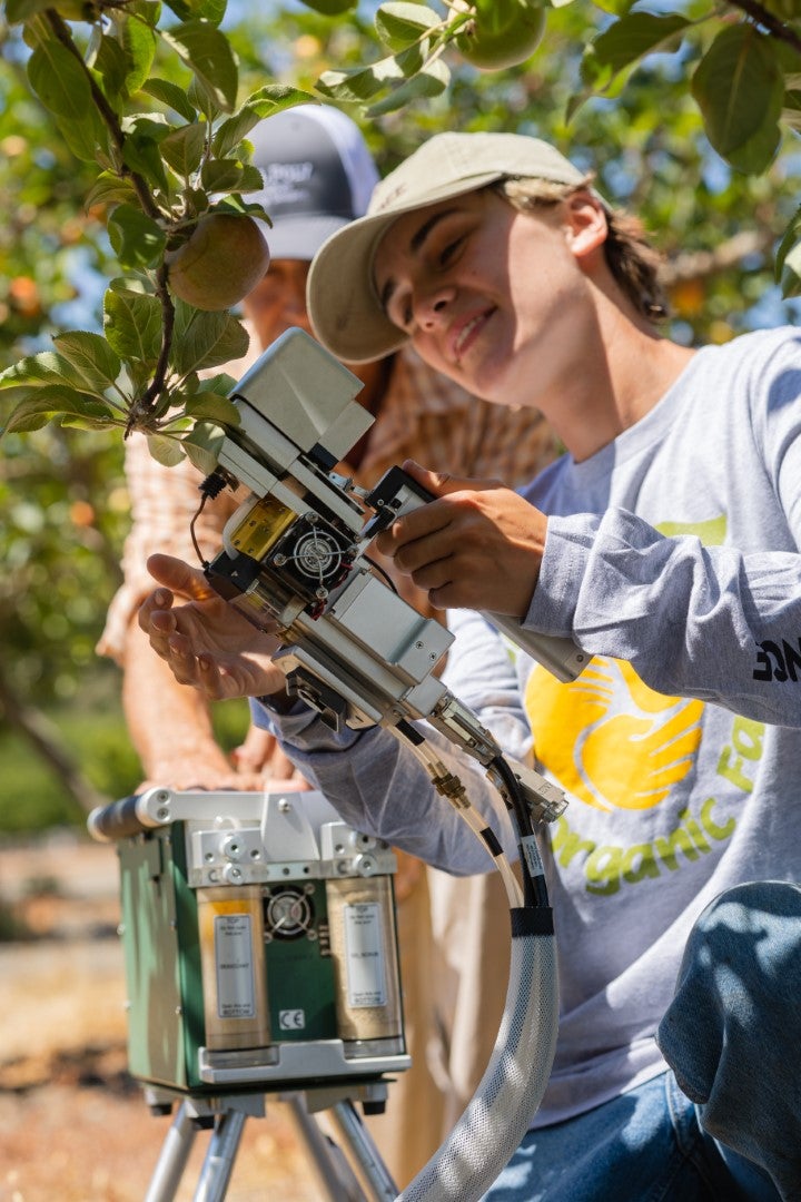 Student operating agricultural technology equipment in an orchard during hands-on plant science or precision agriculture fieldwork.