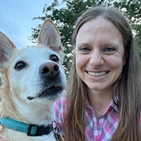 Portrait of a smiling woman posing beside a dog outdoors.