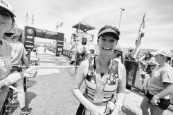 A participant wearing medals smiles at the camera during an outdoor athletic or cycling event.