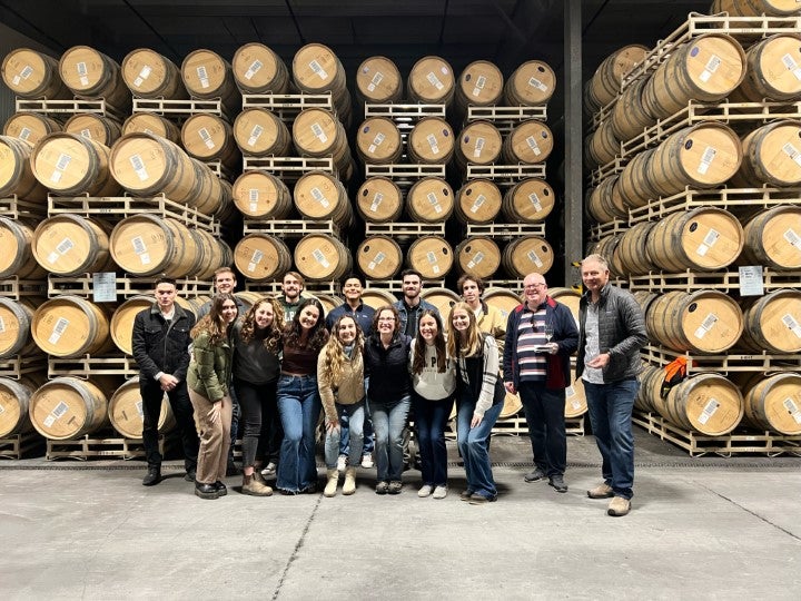 Students and faculty posing inside a wine barrel storage facility during a behind-the-scenes winery operations tour.
