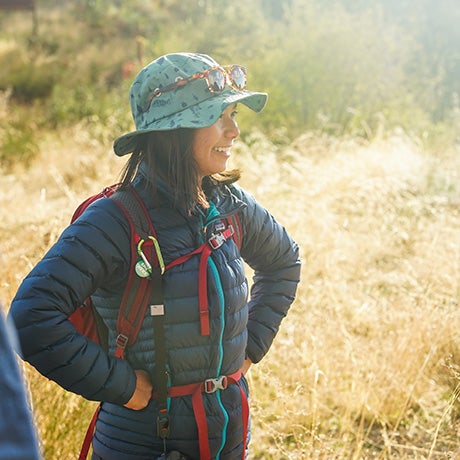 Researcher in outdoor field gear standing in a grassy landscape during an environmental or ecological field study activity.