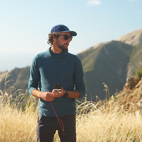 Researcher holding field equipment while standing in a mountainous grassland environment during outdoor scientific data collection or environmental monitoring work.