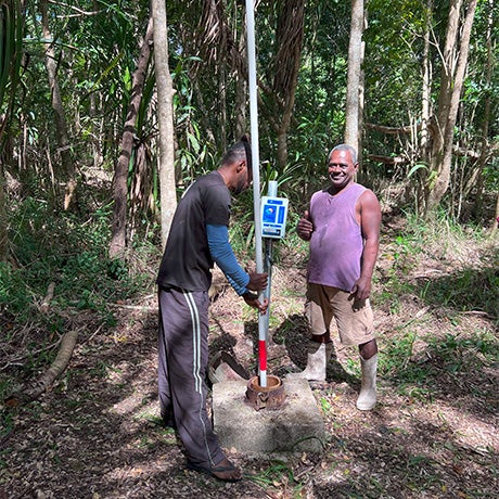 Community members installing and operating a water pump system in a forested outdoor area.