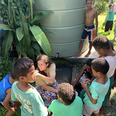 Students and children gathered around a large rainwater collection tank and filtration system during a community water education activity.