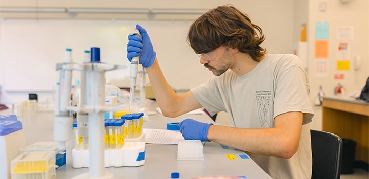 A student uses a pipette while conducting laboratory research at a science workstation.