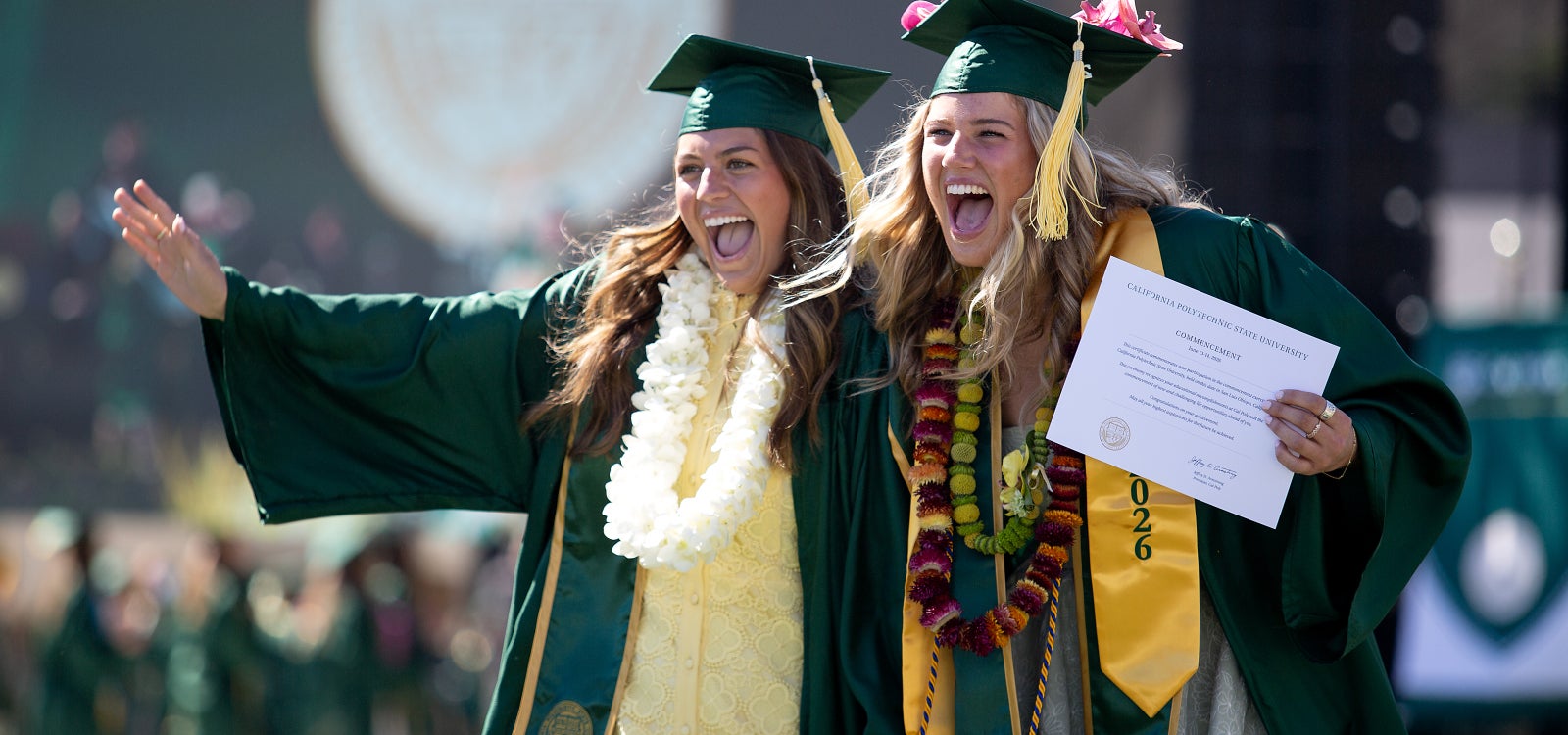 Two students wave to friends and family as they walk down the ramp from the stage during commencement 2026. 