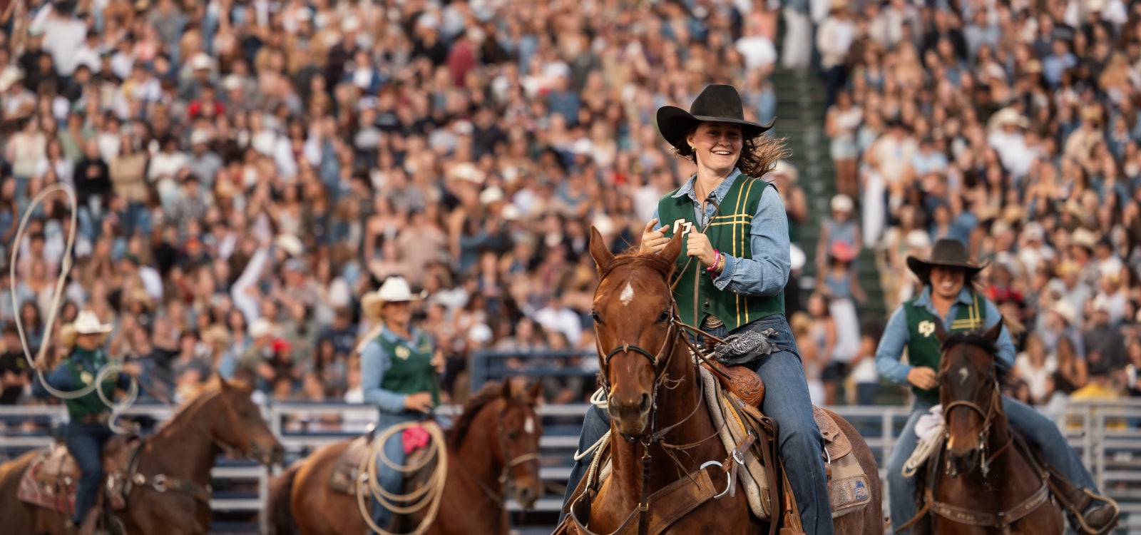 A female rodeo contestant smiles as she rides across the arena in front of a sold out crowd at Spanos Stadium at Cal Poly. 