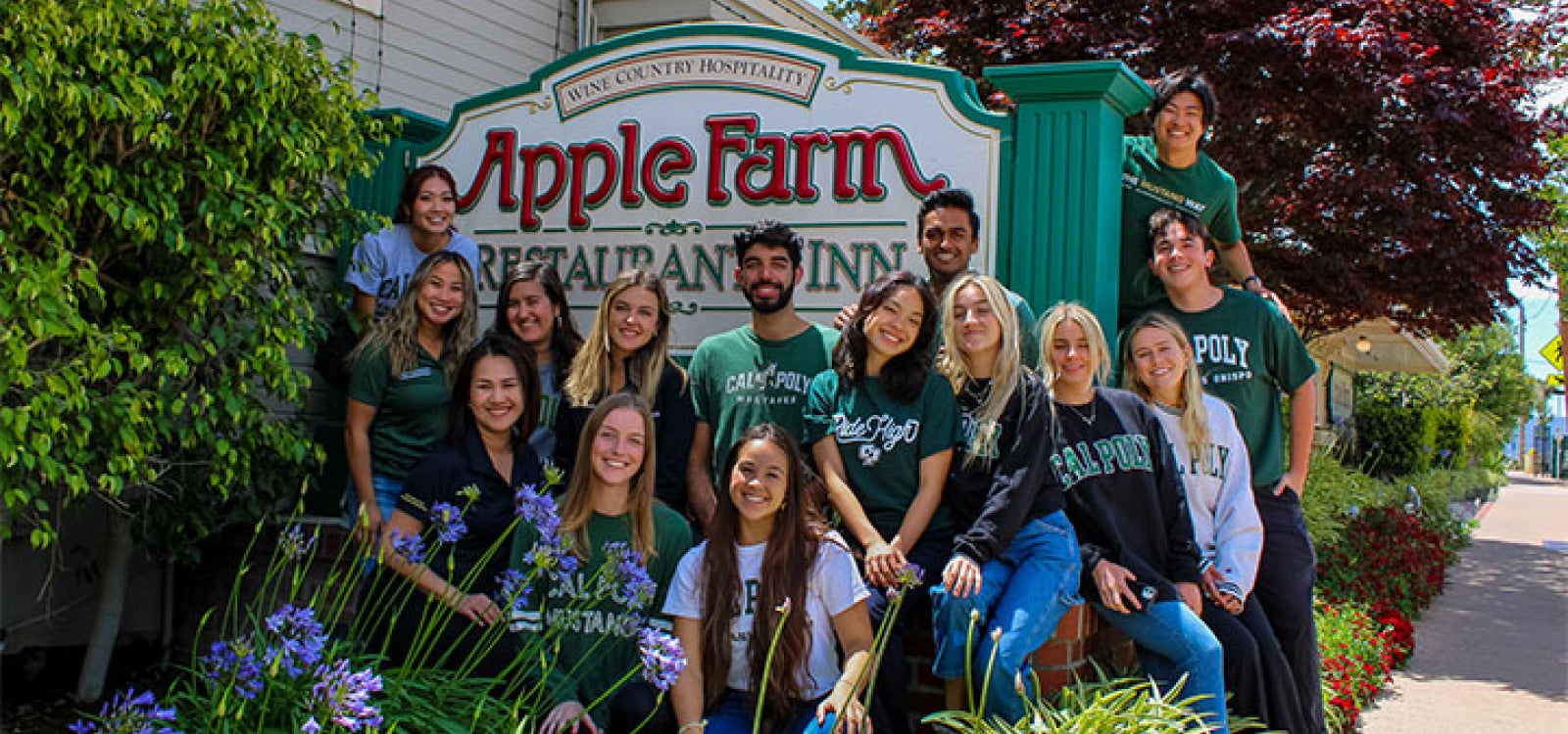 A group of 15 Cal Poly students pose for a photo with the Apple Farm Inn sign in San Luis Obispo.