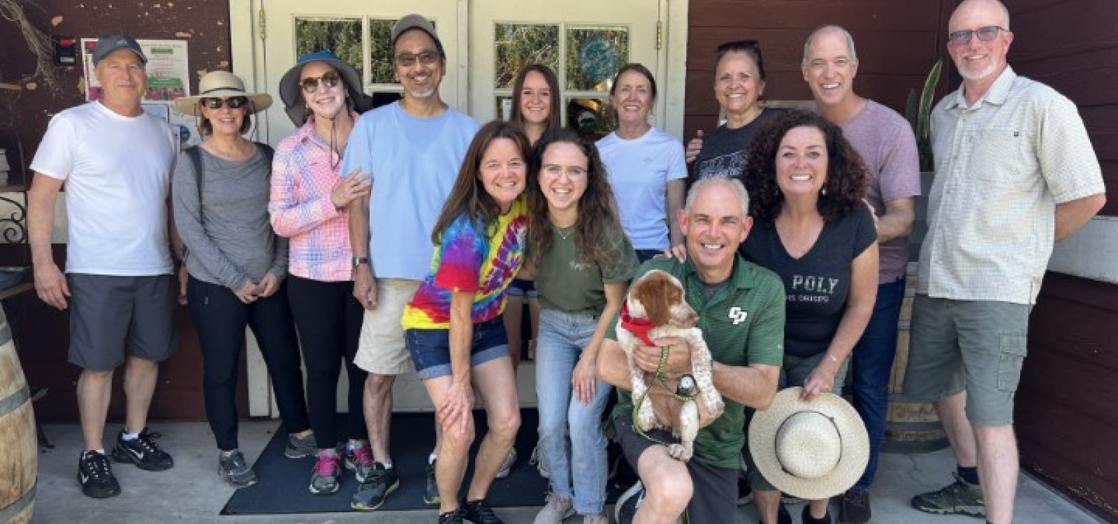 A group of 13 Cal Poly alumni pose for a photo with a dog. 