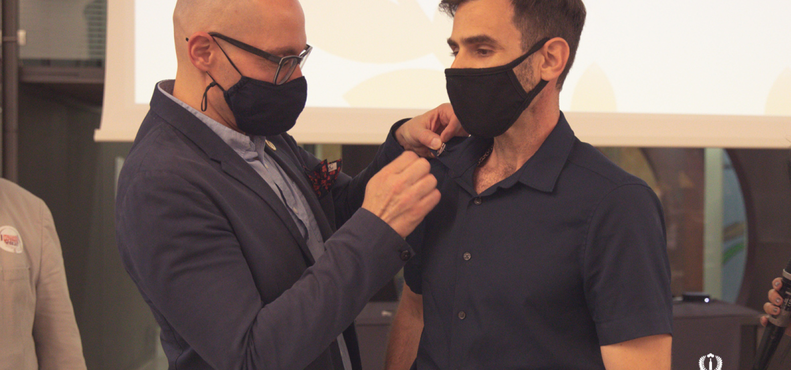 A man in a suit pins an award on the shirt of another man.  