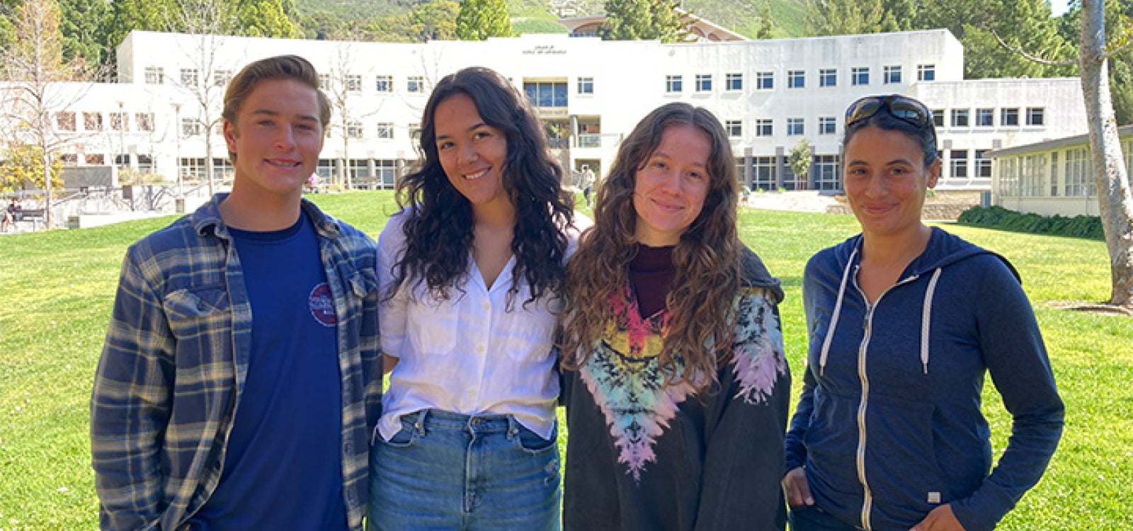 A group of four students posing for a picture in front of a building 