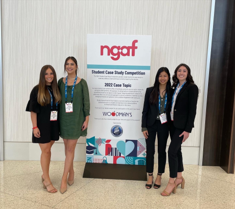 Five students pose smiling beside an NGA Student Case Study Competition banner at a professional conference event.