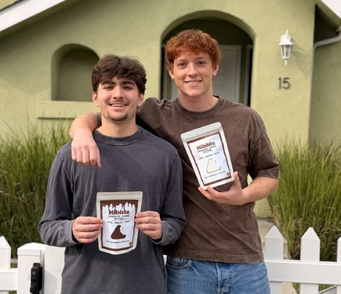 Agricultural business seniors Alex Pope and Josh Van Tassel stand holding packages of Nibble Cheesecake Bites.