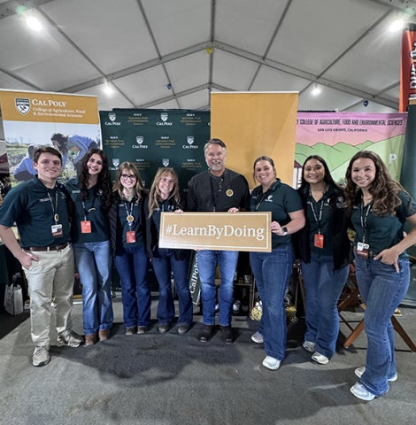 College Dean Brian Horgan and students hold up a sign that reads #Learnbydoing at the World Ag Expo. 