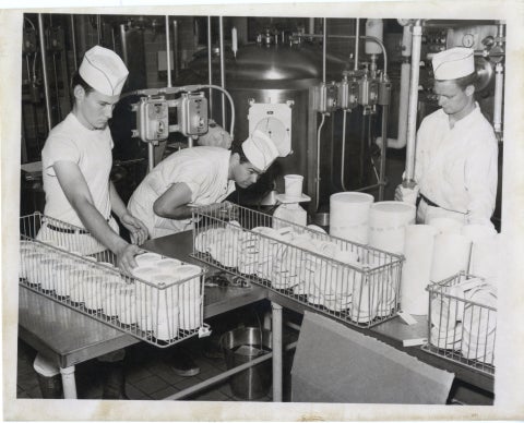 The students are reaching down into a freezer machine (a Cherry-Burrell Nu-Vat) to handle frozen food. They all wear the same uniform, including a white hat, circa 1950s.