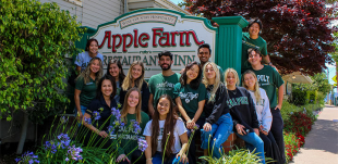 A group of 15 Cal Poly students pose for a photo with the Apple Farm Inn sign in San Luis Obispo.
