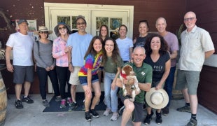 A group of 13 Cal Poly alumni pose for a photo with a dog. 