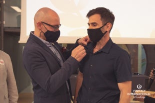 A man in a suit pins an award on the shirt of another man.  