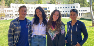A group of four students posing for a picture in front of a building 