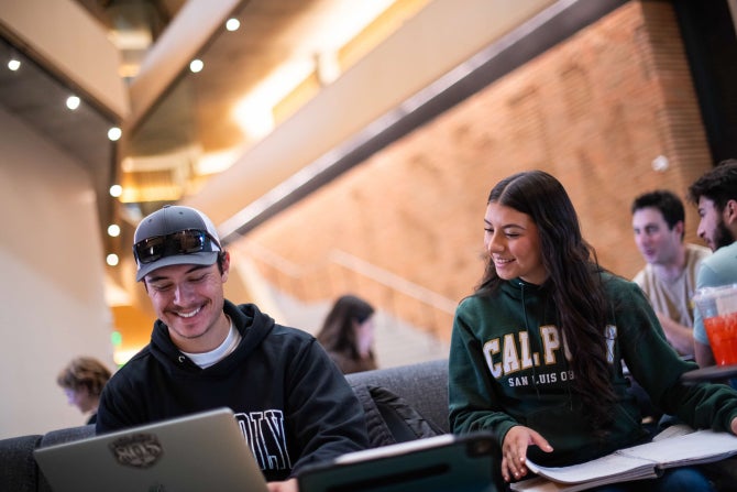 Two students smile while on a laptop computer registering for classes. 