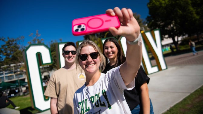 Three students take a selfie in front of the Cal Poly letters. 