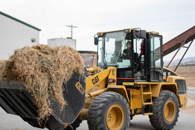 A student drives a tractor with a load of animal feed. 