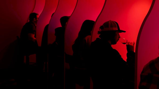 A student smells a glass of wine while sitting with others in a sensory lab with a red light.  