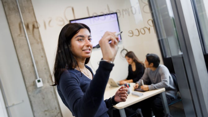 A student writes on a glass window in a study room in the Kennedy Library at Cal Poly. 