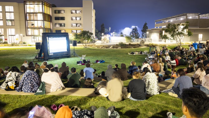 Students sit on the grass and watch a movie in the quad of a residential living community at Cal Poly.