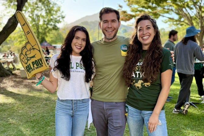 Three college alumni stand together and smile at the camera during a reception. 