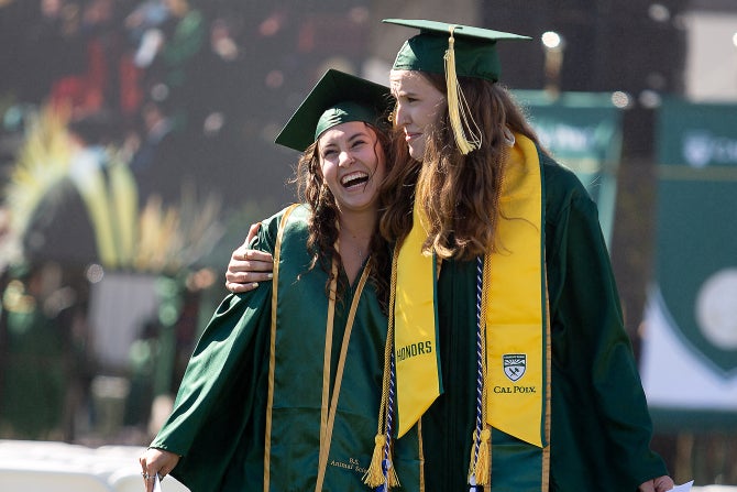 Two students in caps and gowns walk with their arms around each others shoulders after receiving their degree during commencement.  