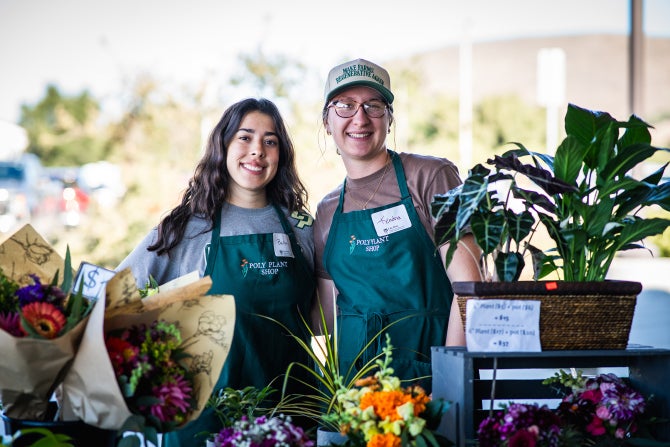 Two students, surrounded by flowers from the Poly Plant Shop, smile at the camera. 