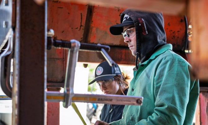 A student works on a laptop while performing engineering work on an agave harvester. 