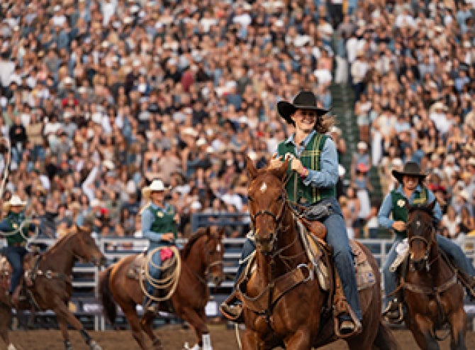 A female rodeo contestant smiles as she rides across the arena in front of a sold out crowd at Spanos Stadium at Cal Poly. 