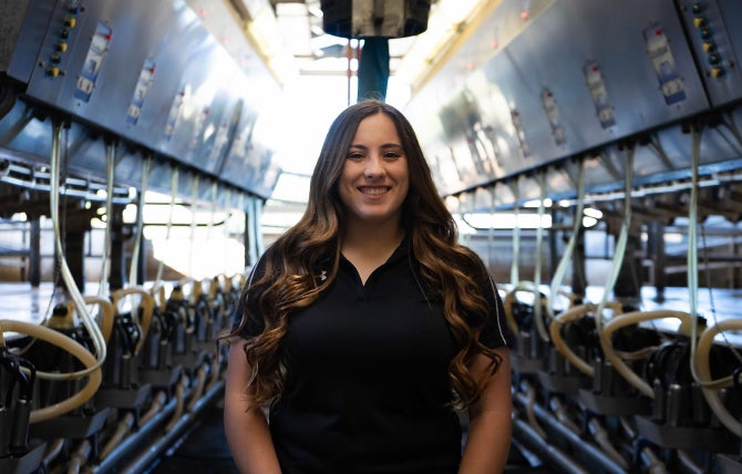 A female Cal Poly dairy science student stands in the milking barn. 