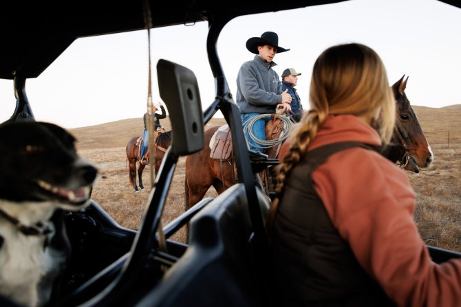 A student on horseback talks with a student in a gator during a cattle drive at the Escuela Ranch.